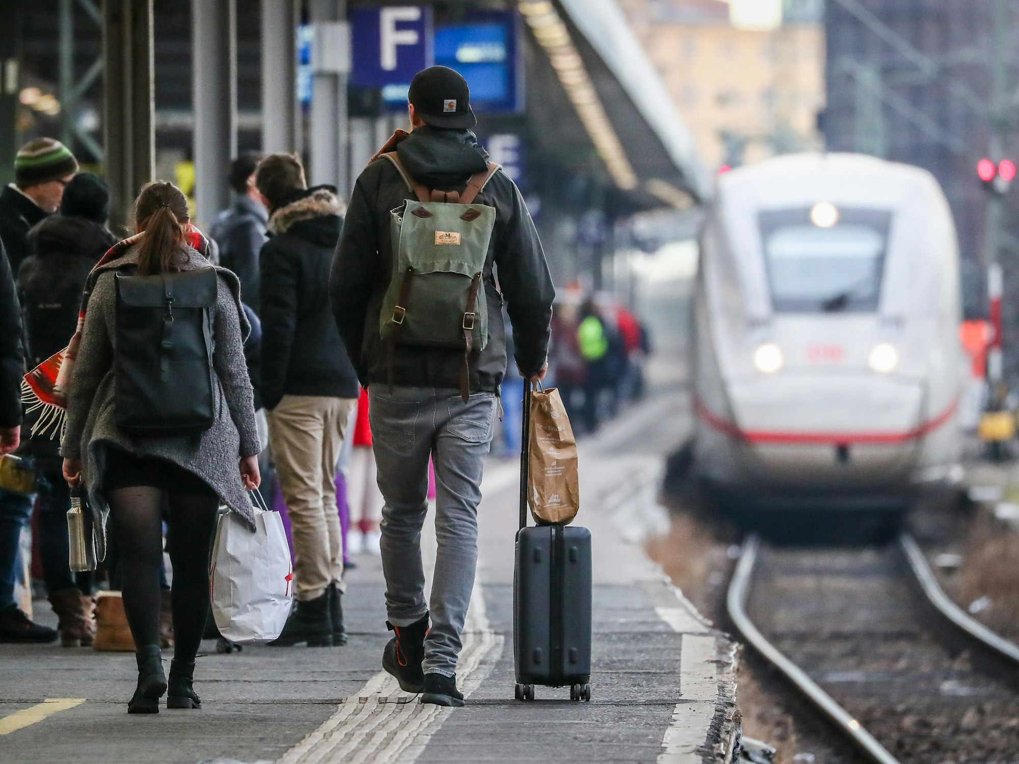 Hier zu sehen, mehrere Personen mit Gepäck auf einem Bahnsteig. Im Hintergrund wartet ein ICE.