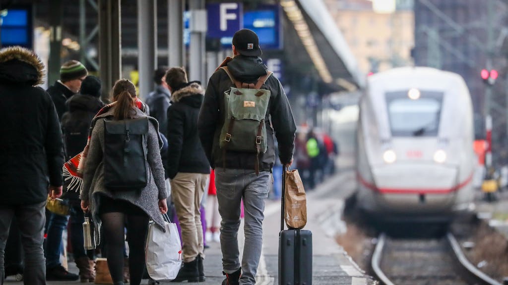 Hier zu sehen, mehrere Personen mit Gepäck auf einem Bahnsteig. Im Hintergrund wartet ein ICE.