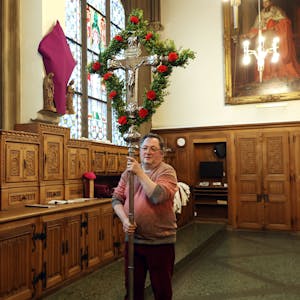 Mann trägt ein mit roten Nelken und Zweigen geschmücktes, großes Silberkreuz vor sich her