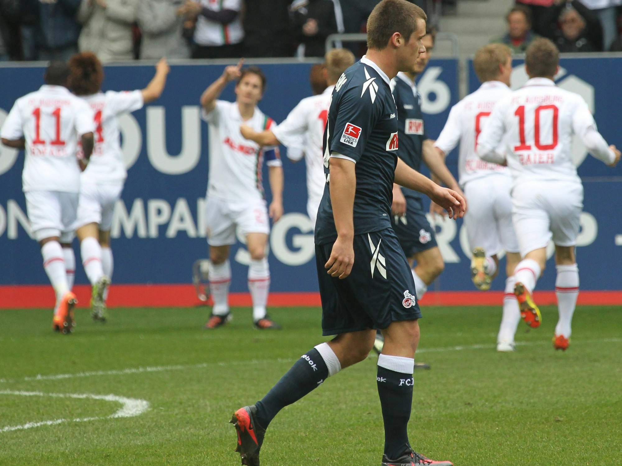 Frust bei Christian Clemens, während die Spieler des FC Augsburg im Hintergrund jubeln.
