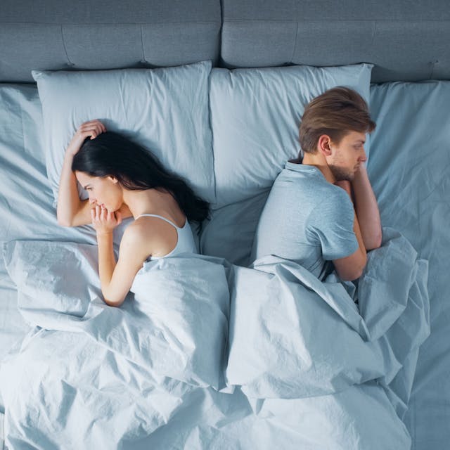 Ein Paar ein Mann und eine Frau liegen mit dem Rücken zueinander im gemeinsamen Bett