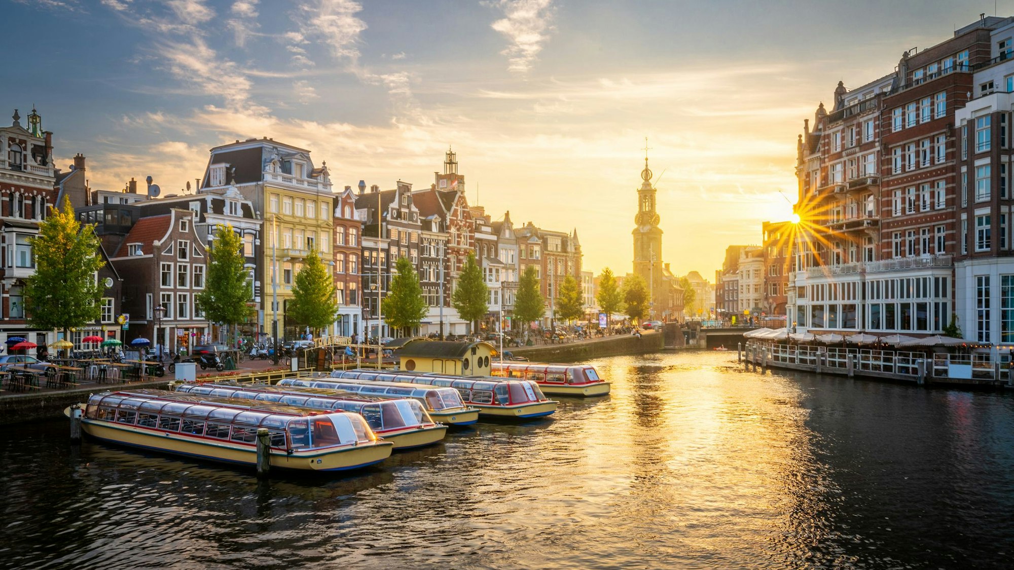 Auf dem Foto sieht man Amsterdam und einen seiner Kanäle im Sonnenuntergang.