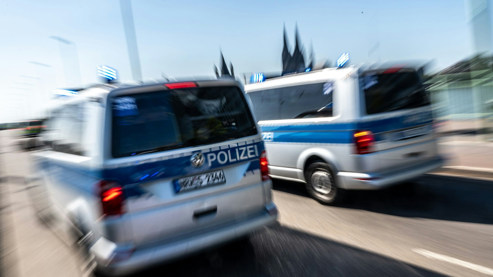 Zwei Polizeifahrzeuge sind mit Blaulicht auf der Deutzer Brücke im Einsatz. Im Hintergrund sind die zwei Türme des Kölner Doms (Symbolbild)