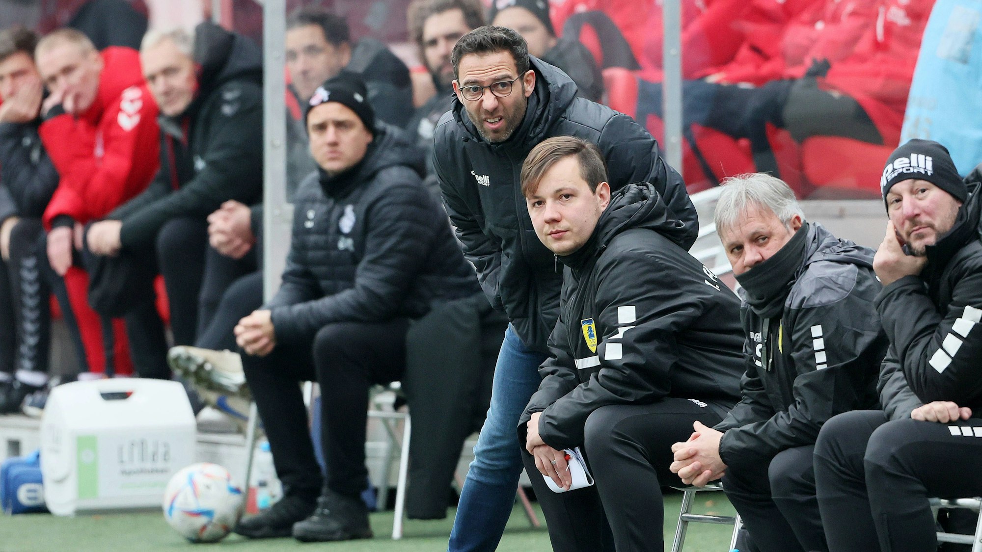 Boris Schommers steht mit anderen Vereinskollegen als Trainer am Spielfeldrand eines Fußballfeldes und verzieht konzentriert das Gesicht.
