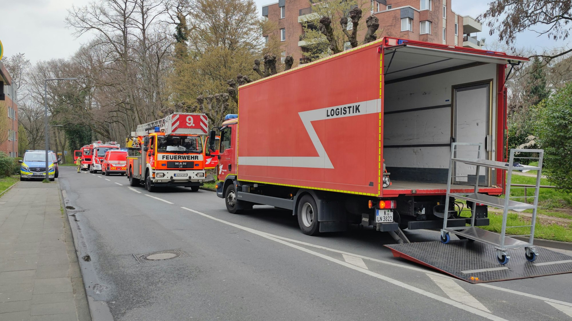 Während des Feuers in einem Mehrfamilienhaus in Dellbrück stehen Feuerwehrfahrzeuge auf der Straße.