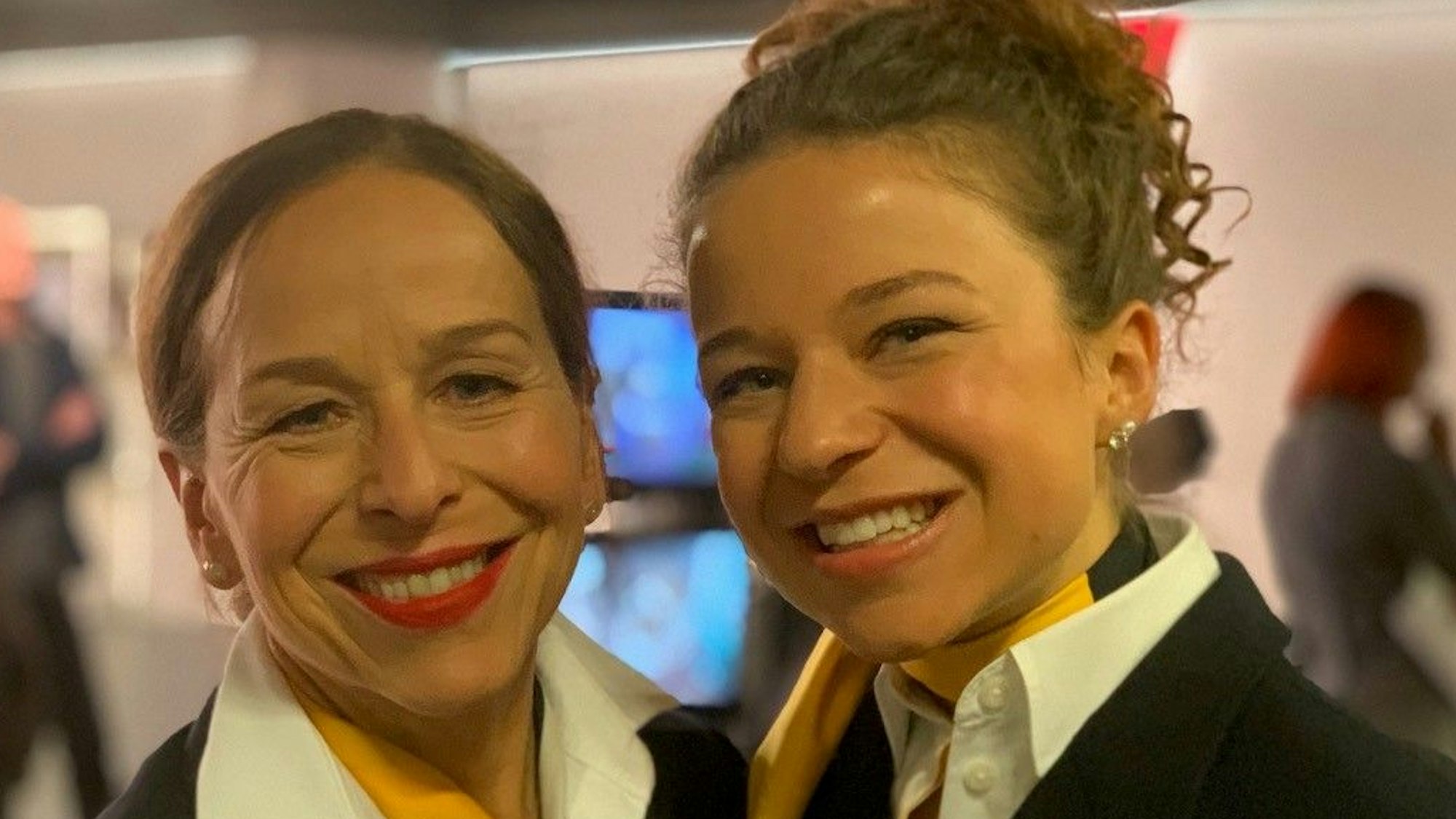 Zwei Frauen in Stewardess-Kleidung lächeln in die Kamera.