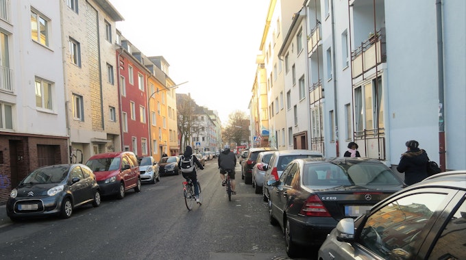 Auf der Straße fahren zwischen geparkten Autos zwei Radfahrer.