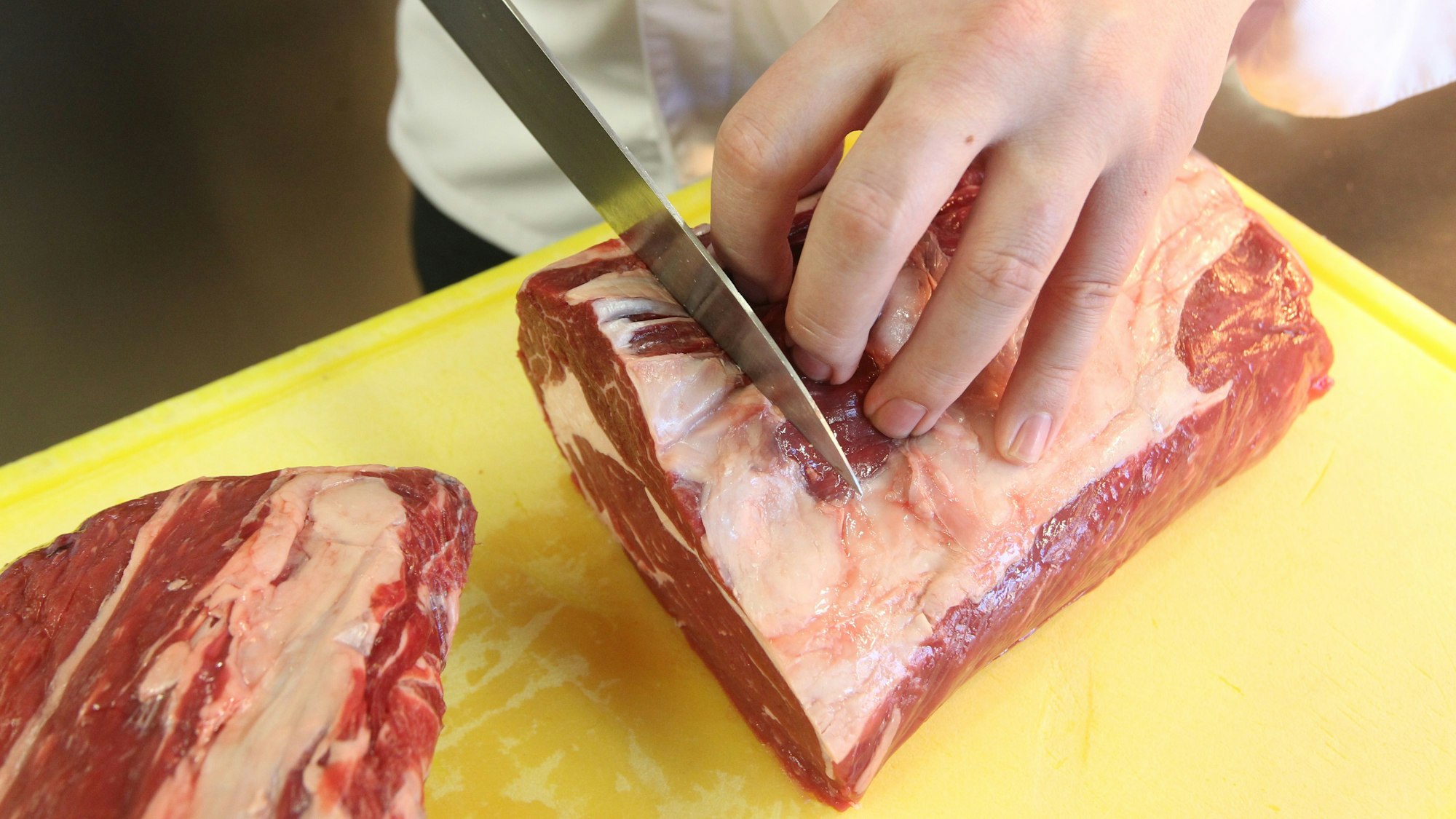 Ein großes Stück Fleisch wird auf einem gelben Brett geschnitten.