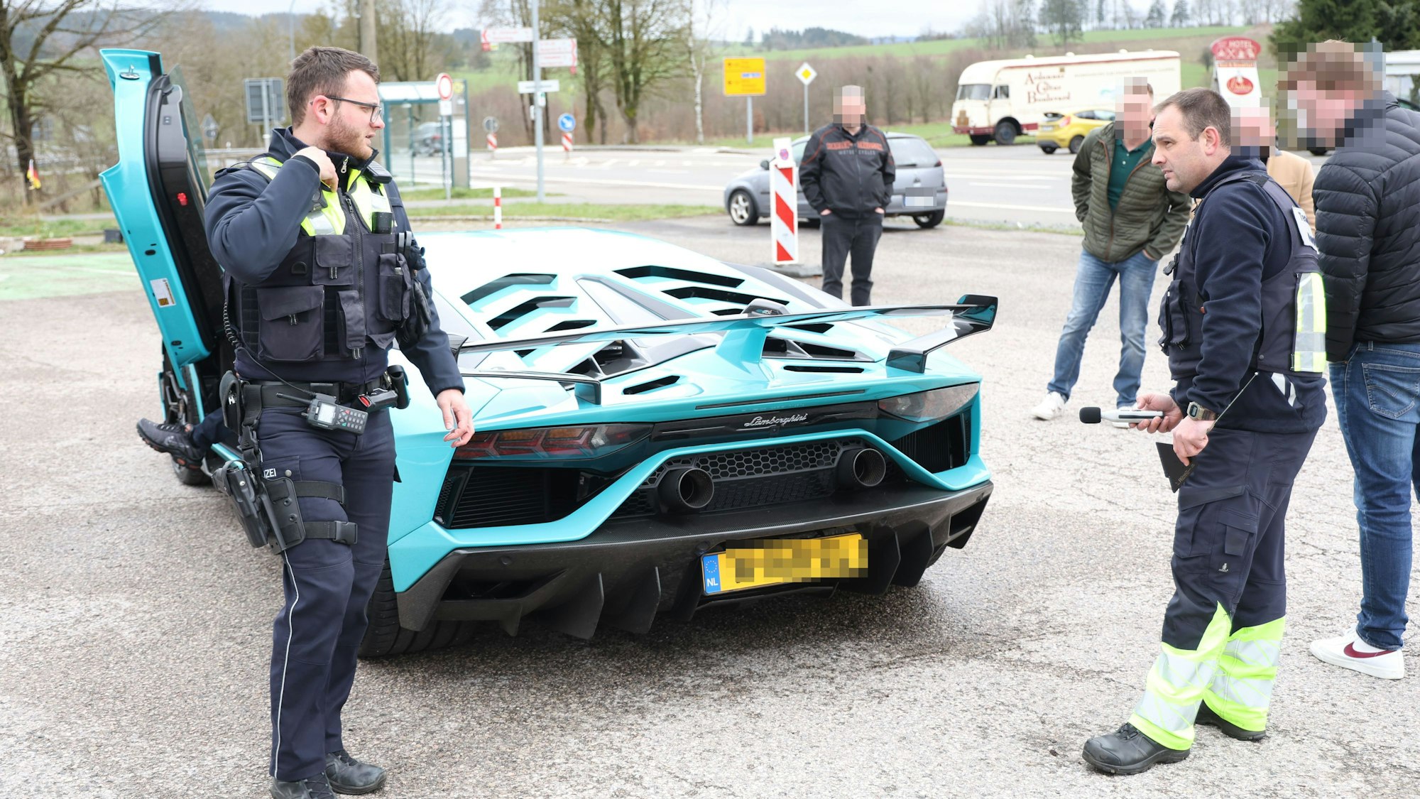 Polizeibeamte und Technikexperten begutachten den hellblauen Lamborghini, dessen Flügeltür an der Fahrerseite geöffnet ist.