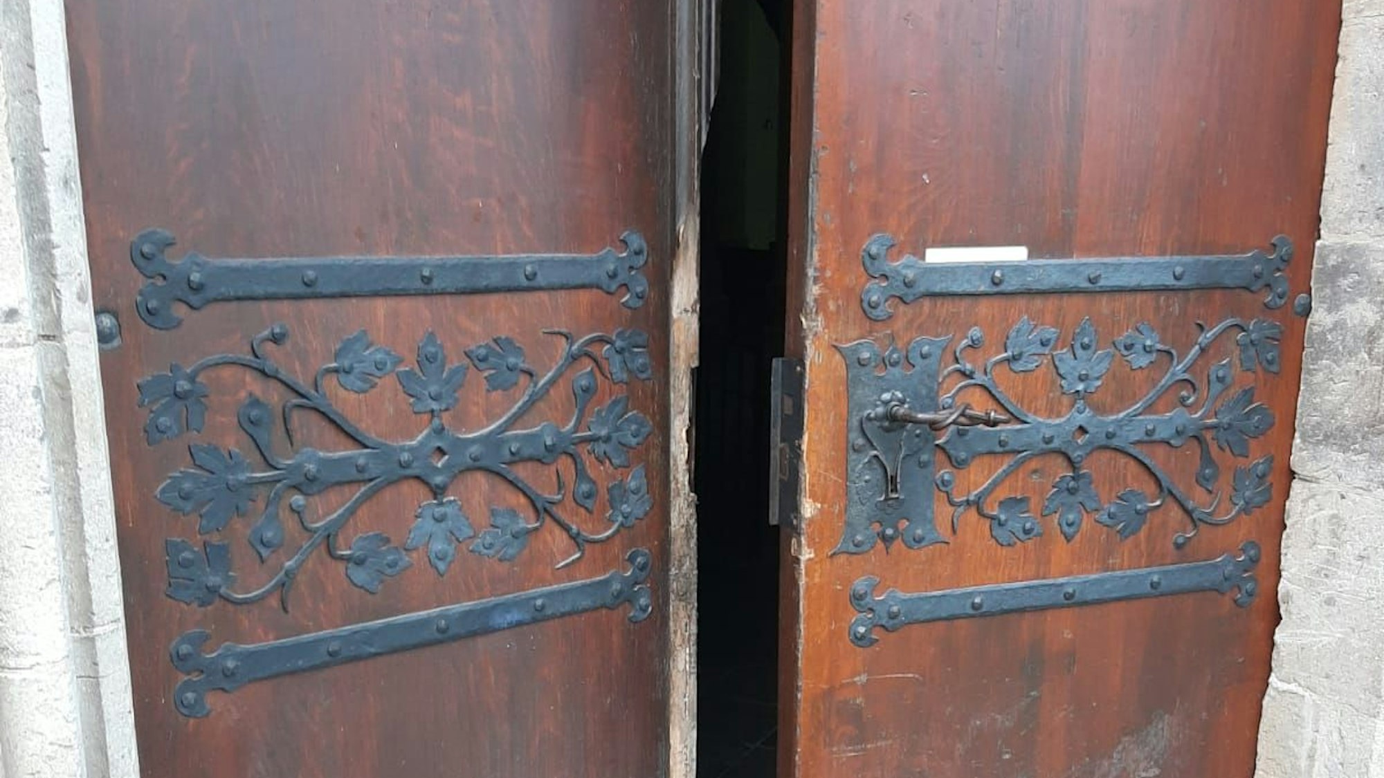 Eine aufgebrochene Holztür mit Metallbeschlägen ist halb geöffnet.