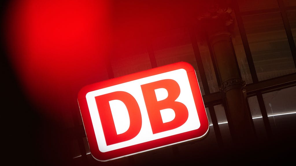 Das Logo der Deutschen Bahn leuchtet an einem Bahnhof.