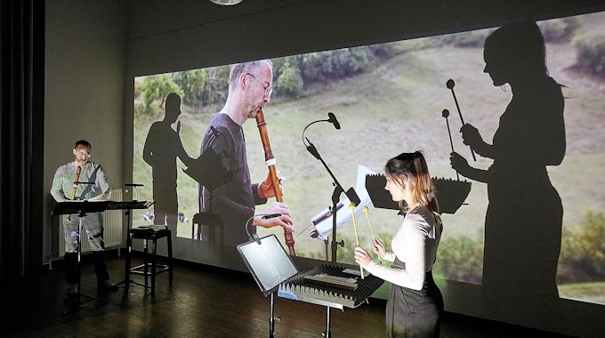 Die beiden Musiker spielen vor einer Videoleinwand. Dort mischen sich ihre Schatten mit dem Film, der sie bei Musikaufnahmen mit dem gleichen Stück auf dem Kalvarienberg bei Alendorf zeigt.