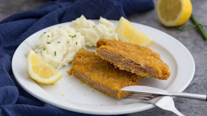 Auf dem Foto sieht man ein veganes Schnitzel auf einem Teller, zusammen mit Kartoffelpüree und einer Zitrone.