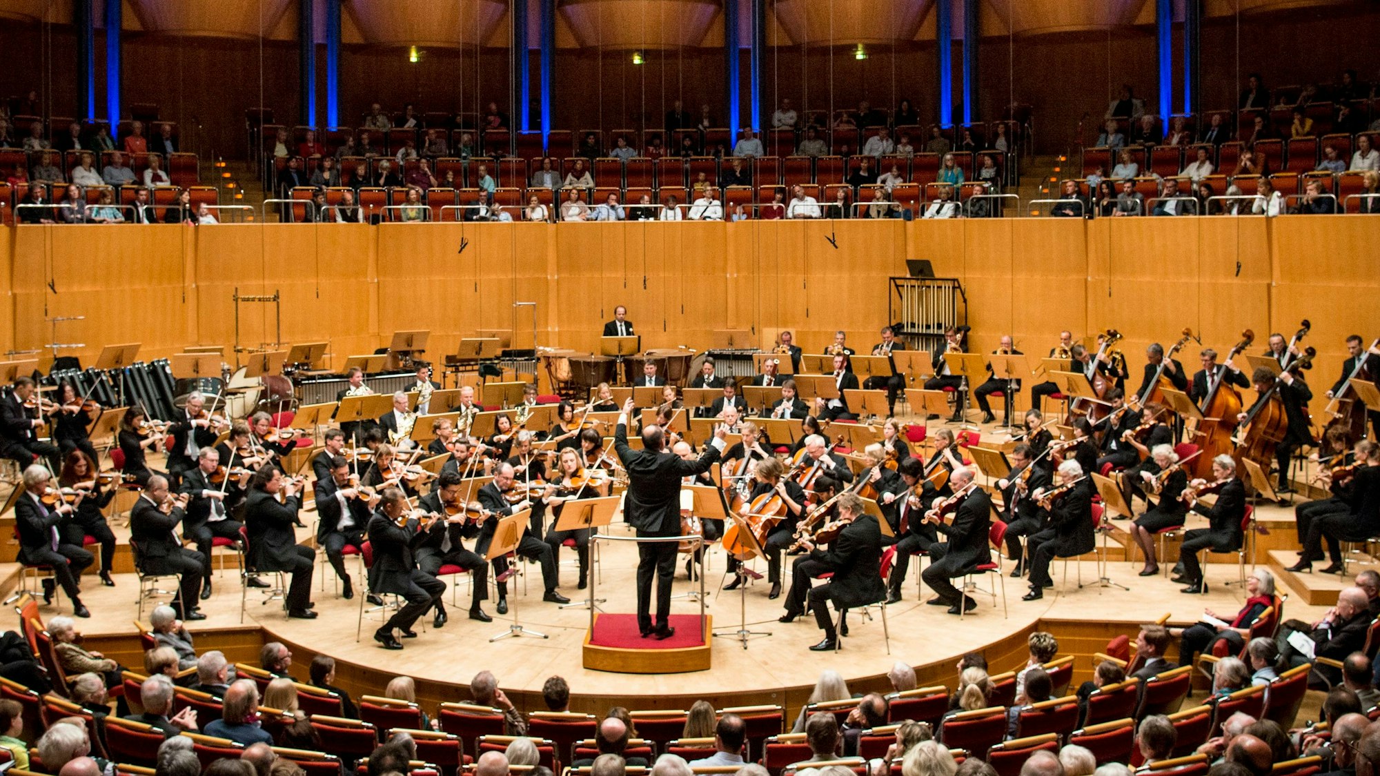 Das Gürzenich-Orchester in der Totalen. Das Orchester spielt in der Kölner Philharmonie, der Dirigent hat die Arme erhoben.
