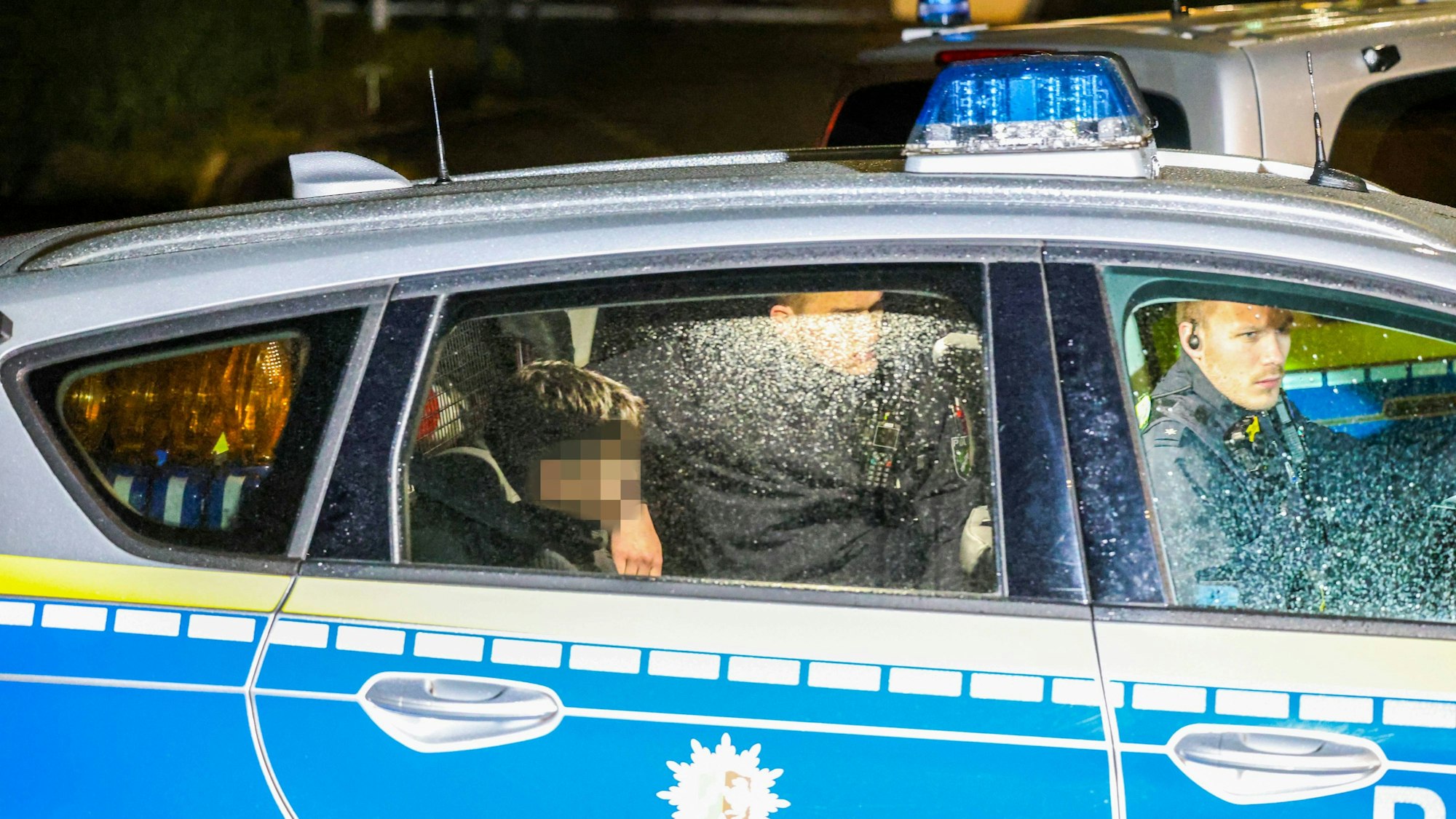 Ein Kind, dessen Gesicht verpixelt ist, sitzt auf dem Rücksitz eines Polizeiwagens.
