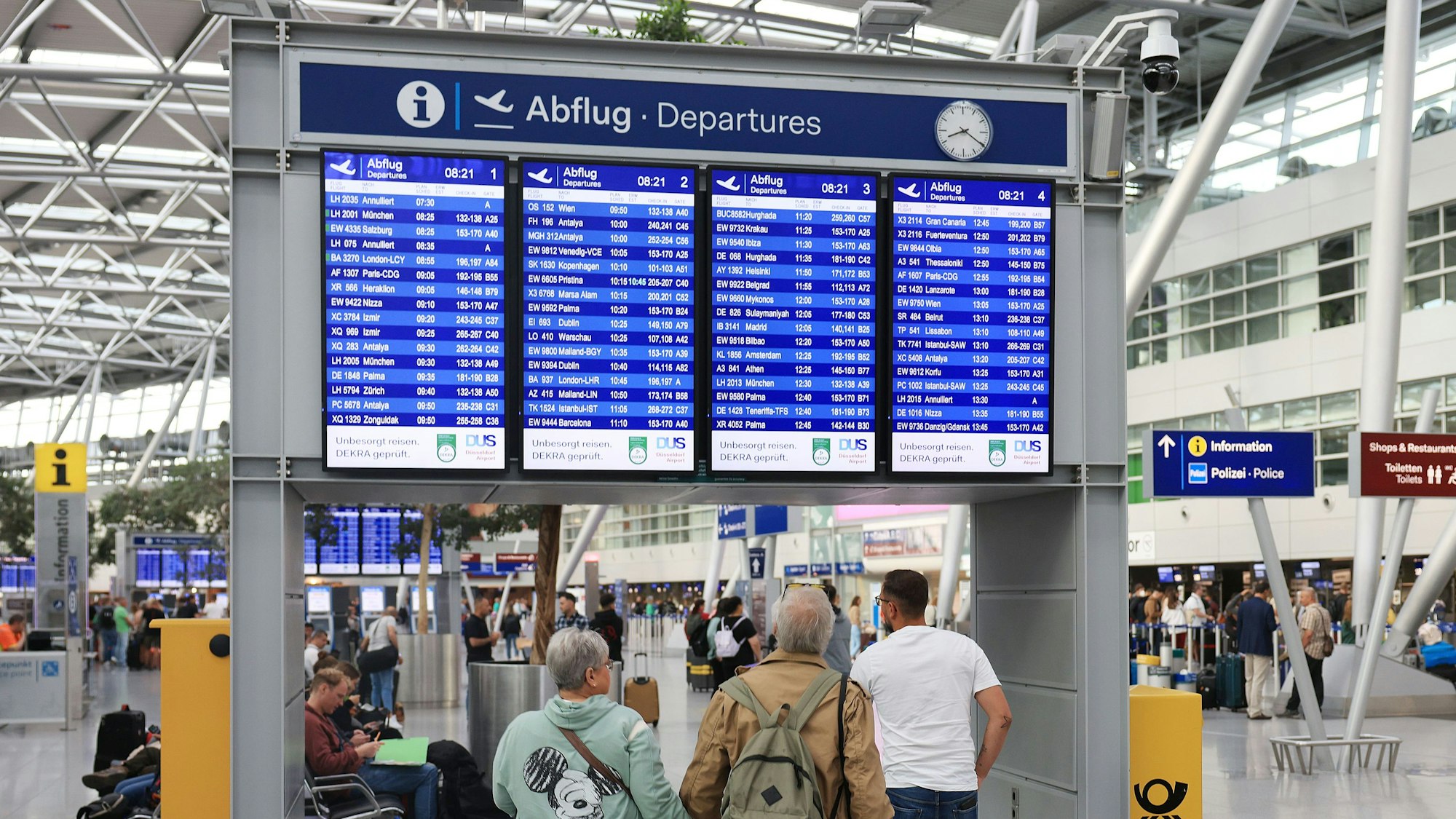 Flugpassagiere stehen vor einer Anzeigetafel im Terminal. 