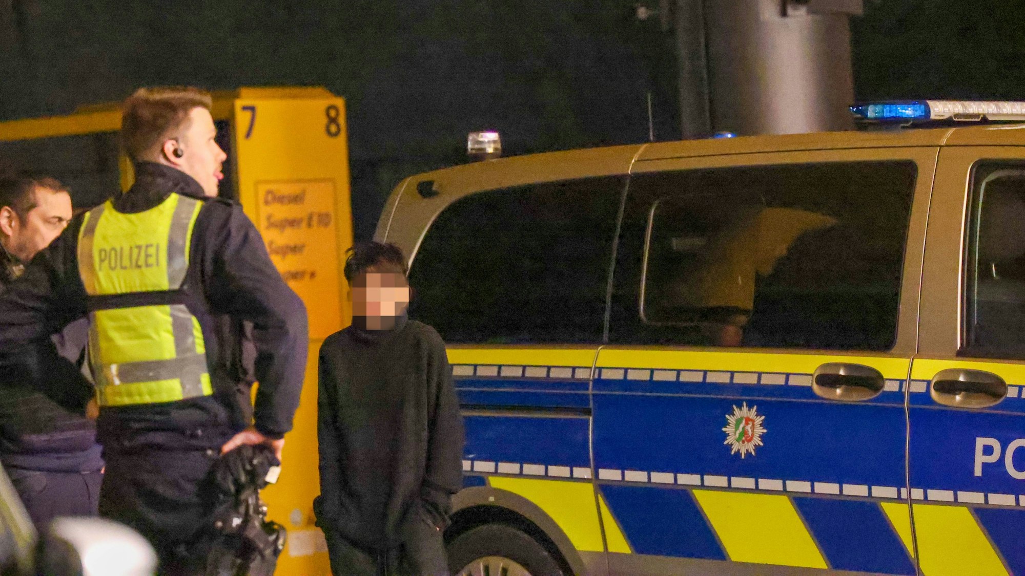 Ein Kind, das Gesicht ist verpixelt, steht neben einem Polizisten und einem Polizeiwagen.