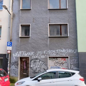 Ein runtergekommenes, unbewohntes Haus in der Kölner Glasstraße 6, mit grauer Fassade, auf die der Spruch „Miethaie zu Fischstäbchen“ gesprüht ist, steht seit mindestens 15 Jahren leer.