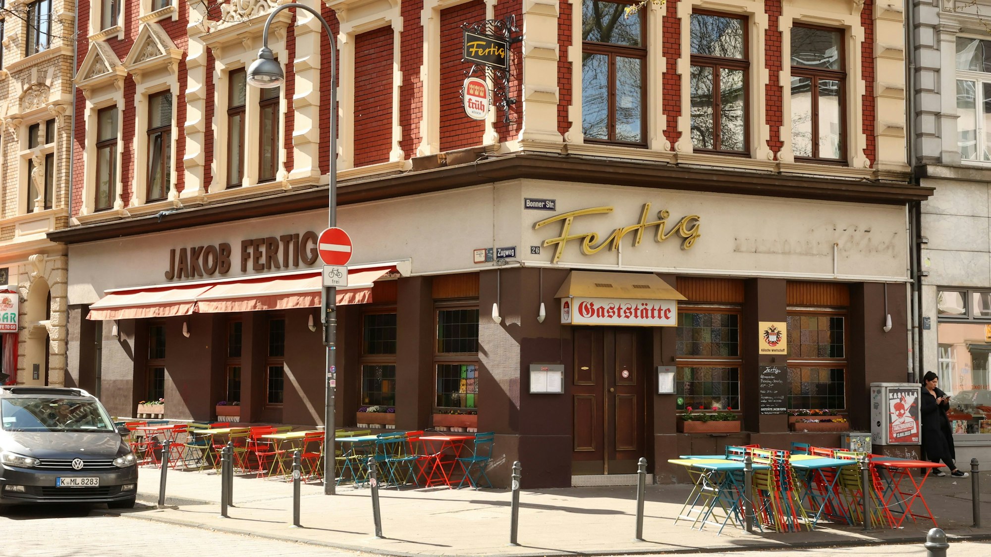 Die Gaststätte Fertig an der Bonner Straße in Köln von außen. Draußen stehen bunte Tische.