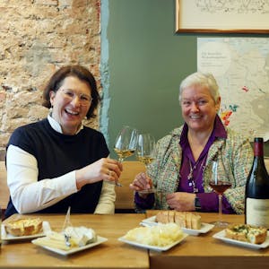 Zwei Frauen sitzen an einem gedeckten Tisch und prosten sich mit Weißwein zu