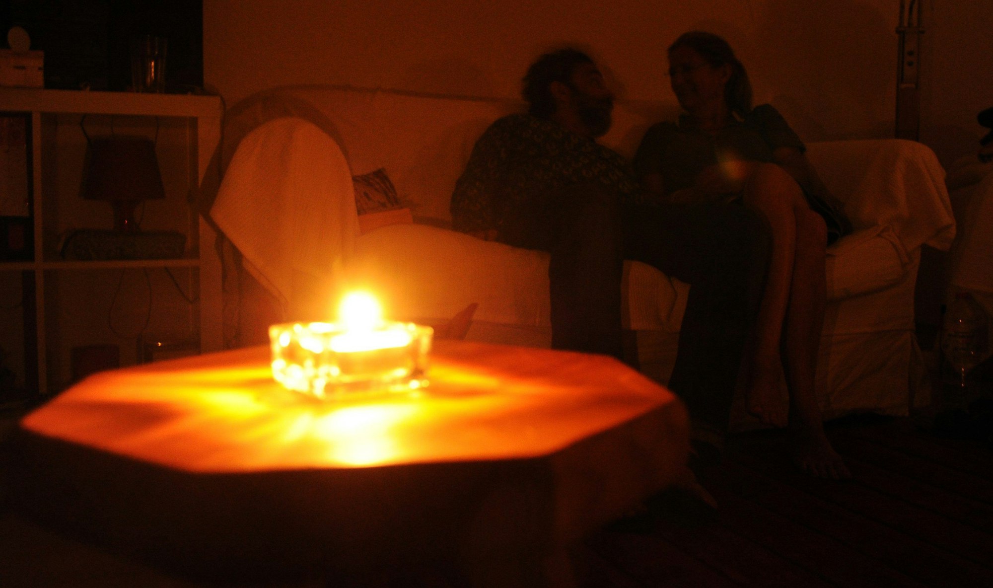 Das Foto zeigt ein Paar, das auf einem Sofa sitzt. Wegen eines Stromausfalls hat es eine Kerze angezündet.