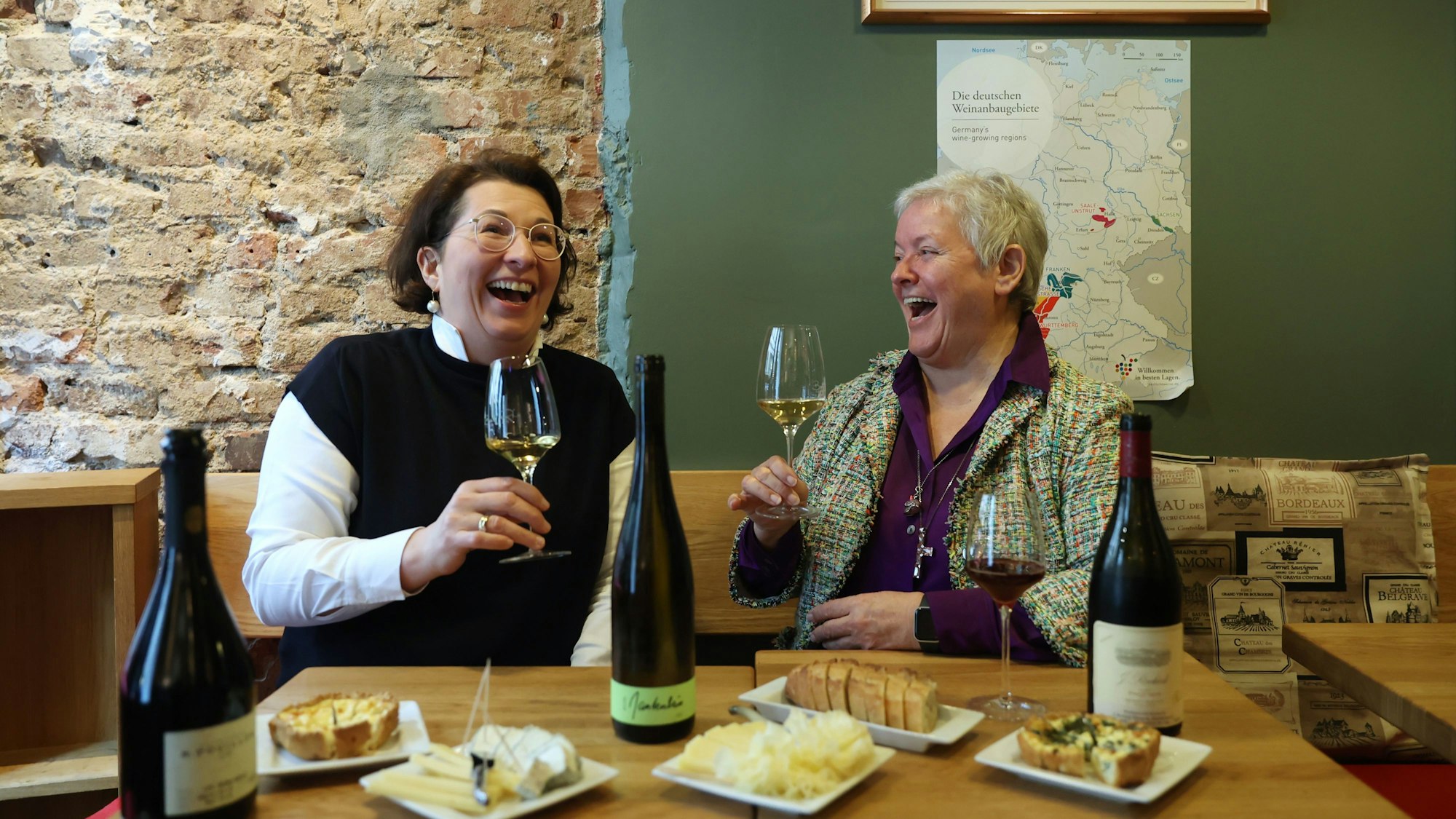 zwei Frauen sitzen mit einem Glas Wein an einem Tisch und lachen