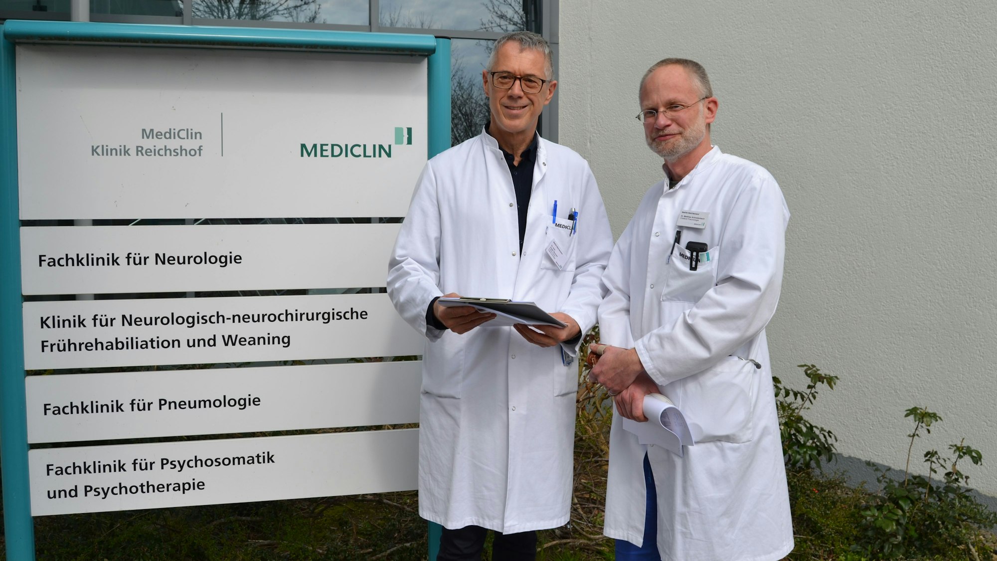 Zwei Ärzte stehen in weißen Kitteln vor dem Eingang der Mediclin-Rehaklinik in Reichshof.