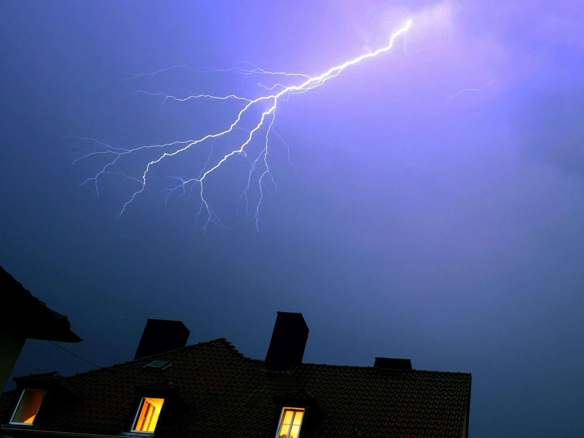 Blitze zucken über einem Haus (Symbolfoto). Ein besonders heftiger Blitz entlud sich am Mittwochabend über Köln-Niehl.