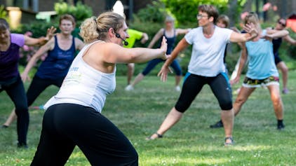 Das Bild zeigt eine Gruppe mit Fitnesstrainerin bei Sport im Park.