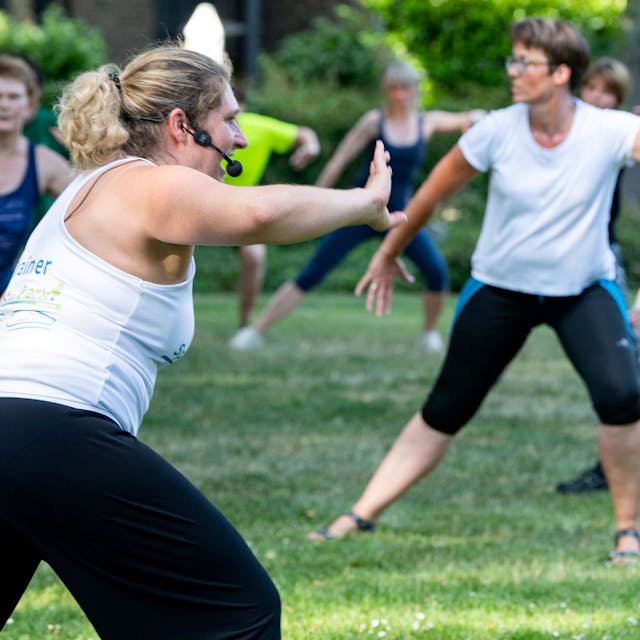 Das Bild zeigt eine Gruppe mit Fitnesstrainerin bei Sport im Park.