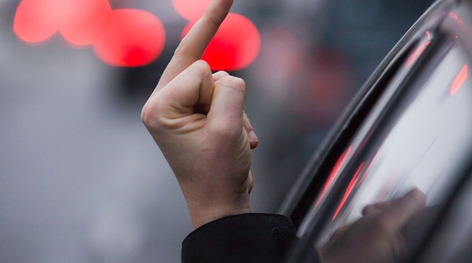 Ein Autofahrer streckt die Hand aus dem Fenster und zeigt den Mittelfinger.&nbsp;