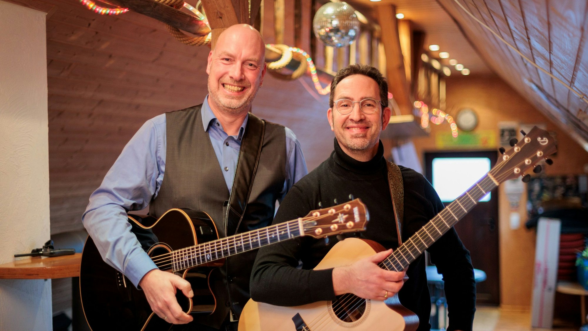 Die beiden Männer posieren mit ihren Gitarren und blicken lächelnd in die Kamera.
