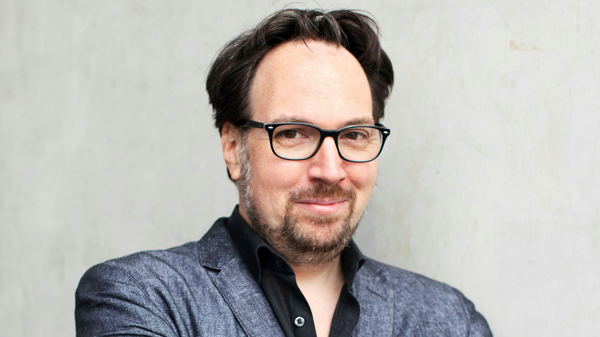 Der Autor Carsten Henn trägt einen dunkelgrauen Anzug und blickt in die Kamera.