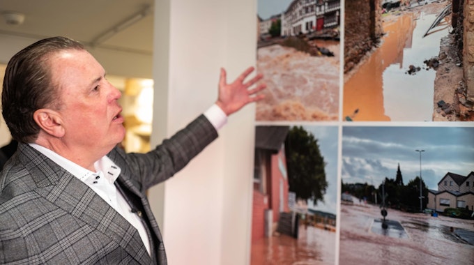 Marc Brucherseifer, Geschäftsführer des City Outlets, deutet auf einige Bilder, die nach der Flutkatastrophe in Bad Münstereifel entstanden sind.