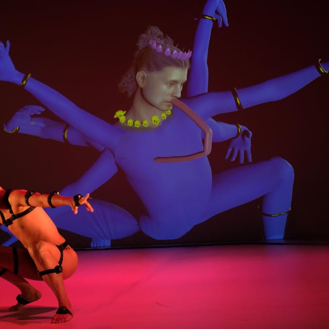 Ein Tänzer aus Singapur in Lederriemen tanzt vor einer Videoinstallation, die eine singapurische Gottheit persifliert.
