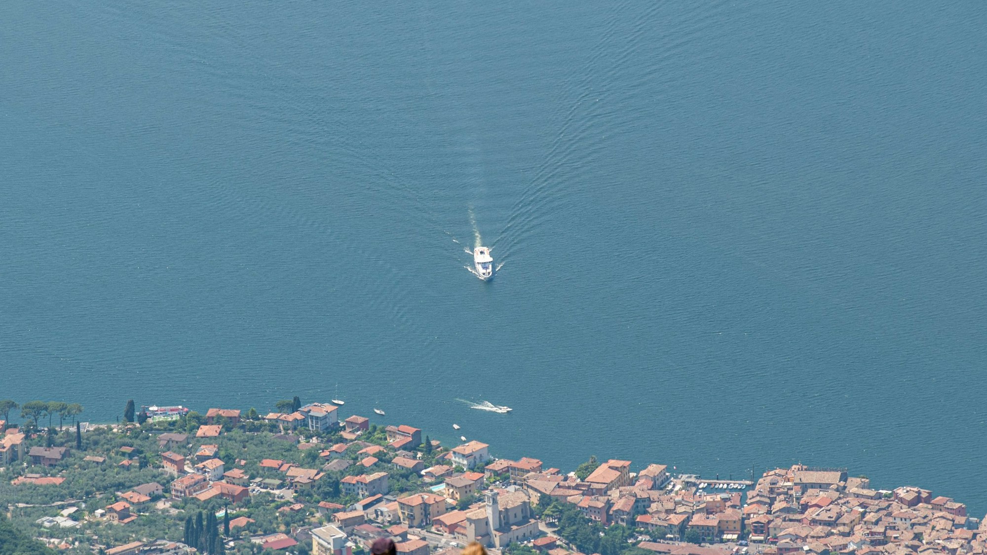 Blick vom Berg Monte Baldo auf den Gardasee und den Ort Malcesine. Auf dem See ist ein weißes Boot unterwegs.