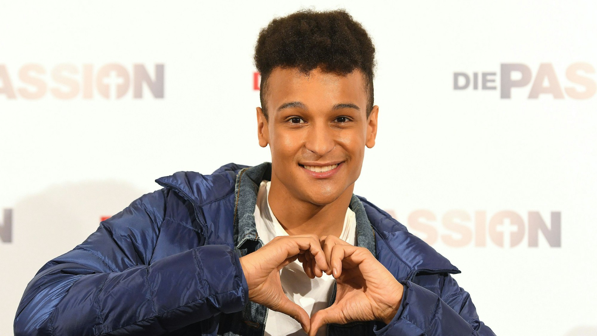 Prince Damien, Sänger nach der Pressekonferenz zum RTL Musik-Live-Event „Die Passion“. Er formt mit seinen Händen ein Herz.