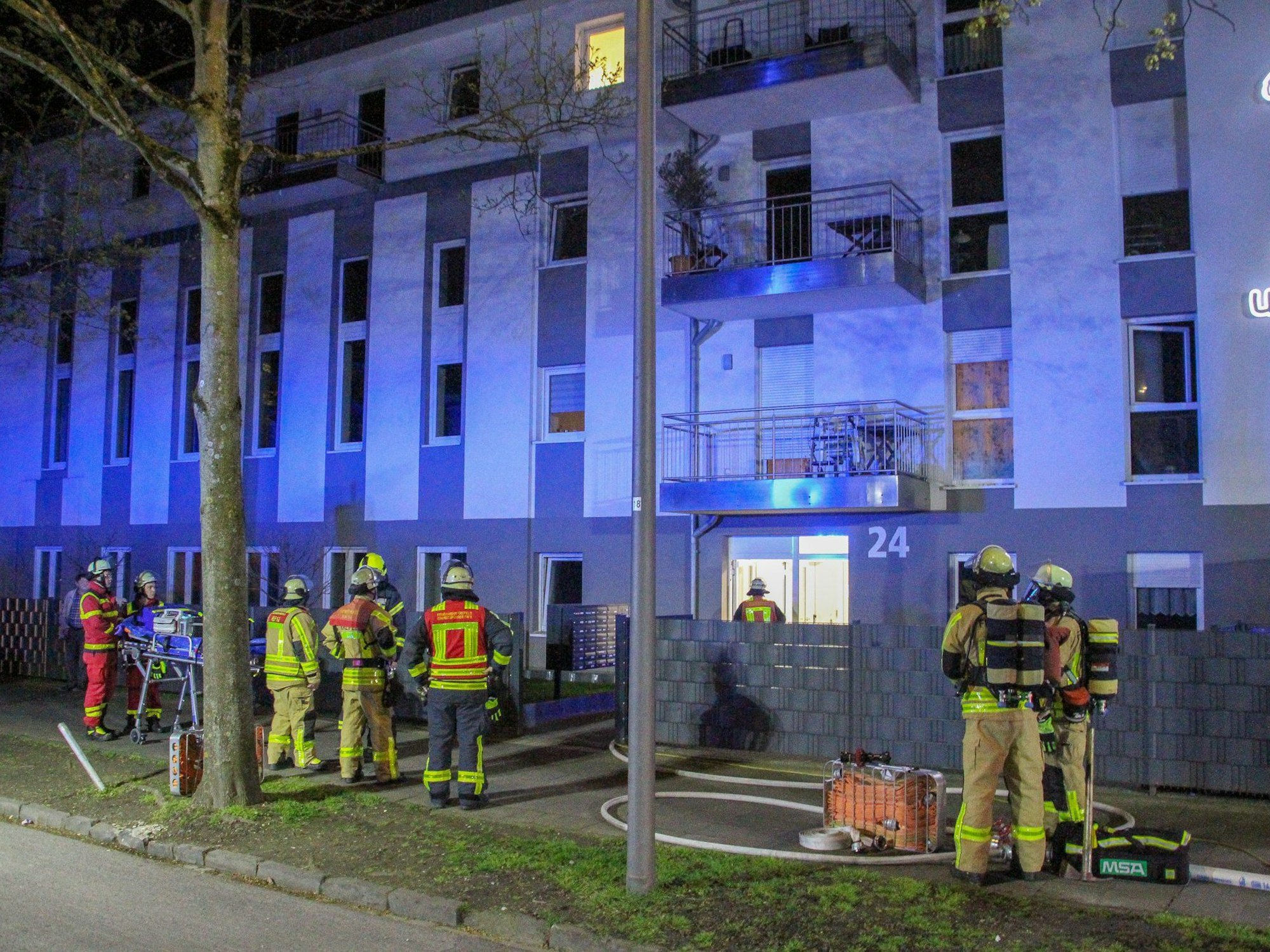 Feuerwehrleute und Rettungskräfte stehen vor einem Haus für betreutes Wohnen in Krefeld, in dem ein Brand ausgebrochen war. Eine Bewohnerin kam bei dem Brand ums Leben.