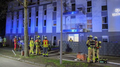 Feuerwehrleute und Rettungskräfte stehen vor einem Haus für betreutes Wohnen in Krefeld, in dem ein Brand ausgebrochen war. Eine Bewohnerin kam bei dem Brand ums Leben.