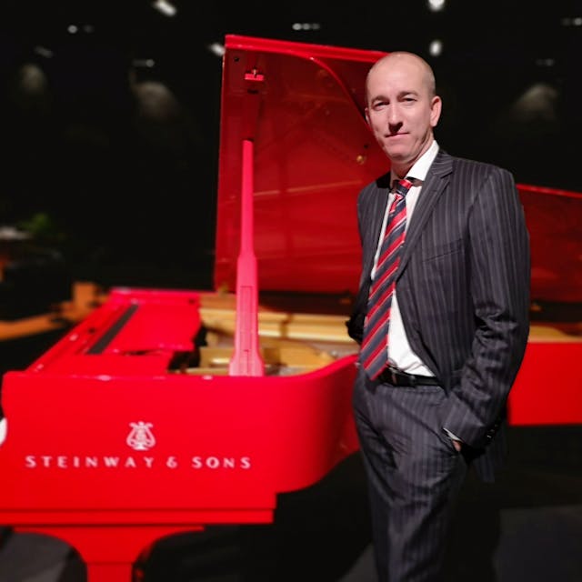 Der amerikanische Pianist Chris Hopkins spielt am 1. Mai in der Ülepooz. Er steht im Anzug vor einem roten Flügel.