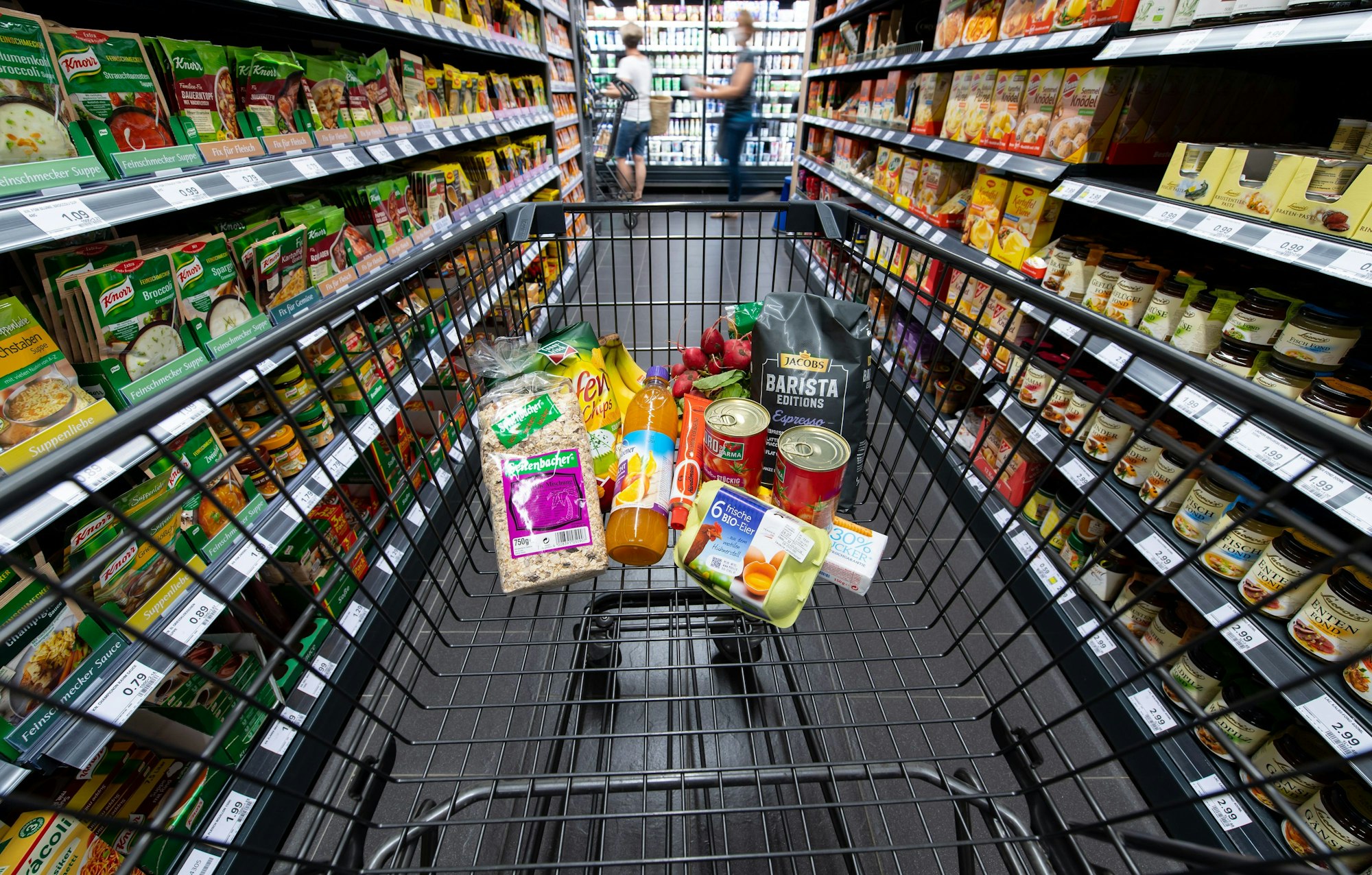 Ein Einkaufswagen mit Produkten zwischen zwei Supermarktregalen.