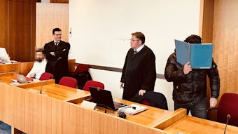 Ein Angeklagter steht neben seinen Anwälten im Gerichtssaal.