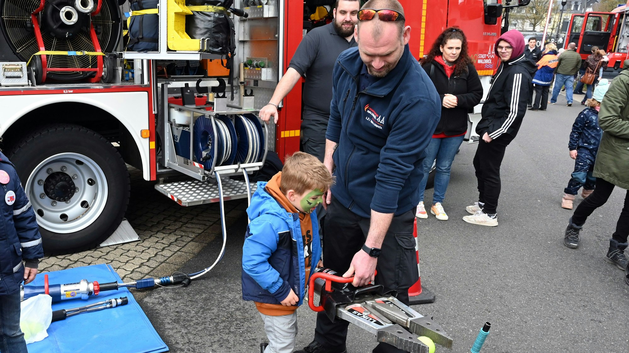 Ein Feuerwehrmann zeigt einem Kind, wie ein Hydraulikspreizer funktioniert.