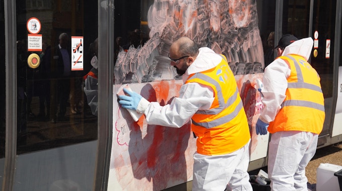 Mitarbeiter einer Fachfirma reinigen eine mit Graffiti beschmierte Stadtbahn.