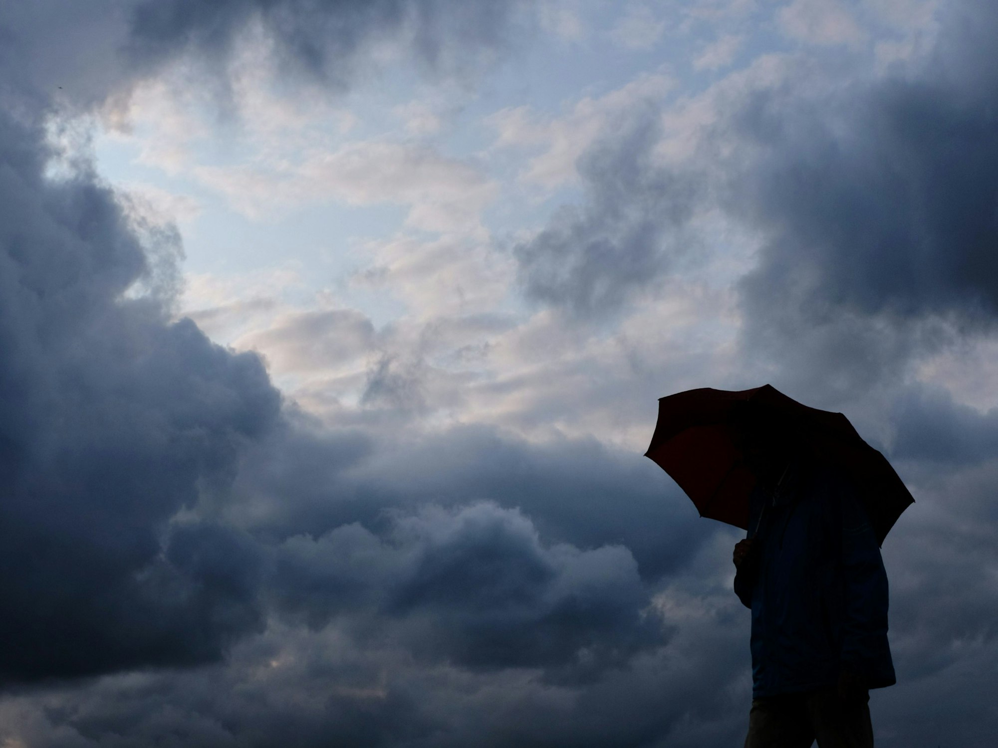 Ein Mann geht mit einem Regenschirm vor aufziehenden dunklen Wolken spazieren.