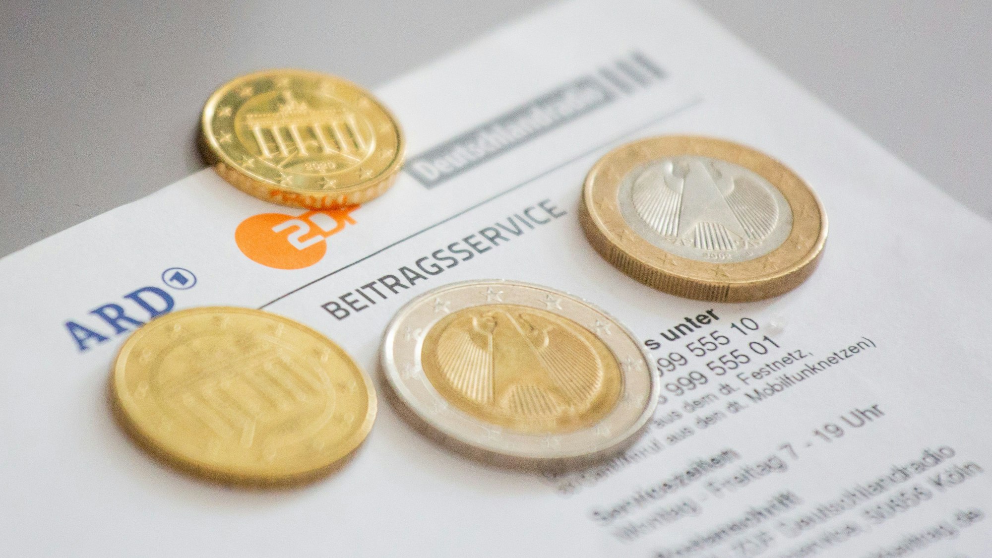 Euromünzen liegen auf einem Anschreiben zur Anmeldung für die Rundfunkgebühren, neben den Logo von ARD, ZDF und Deutschlandfunk.