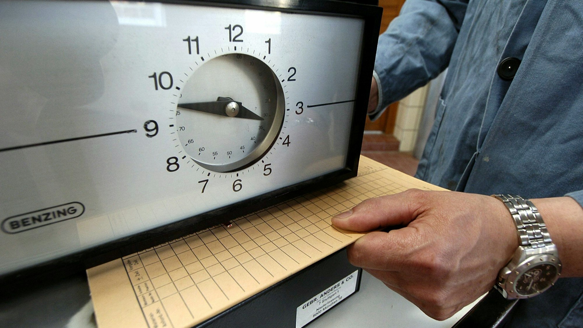 Eine Karte zur Arbeitszeiterfassung wird in einem Betrieb unter eine Stechuhr gelegt.