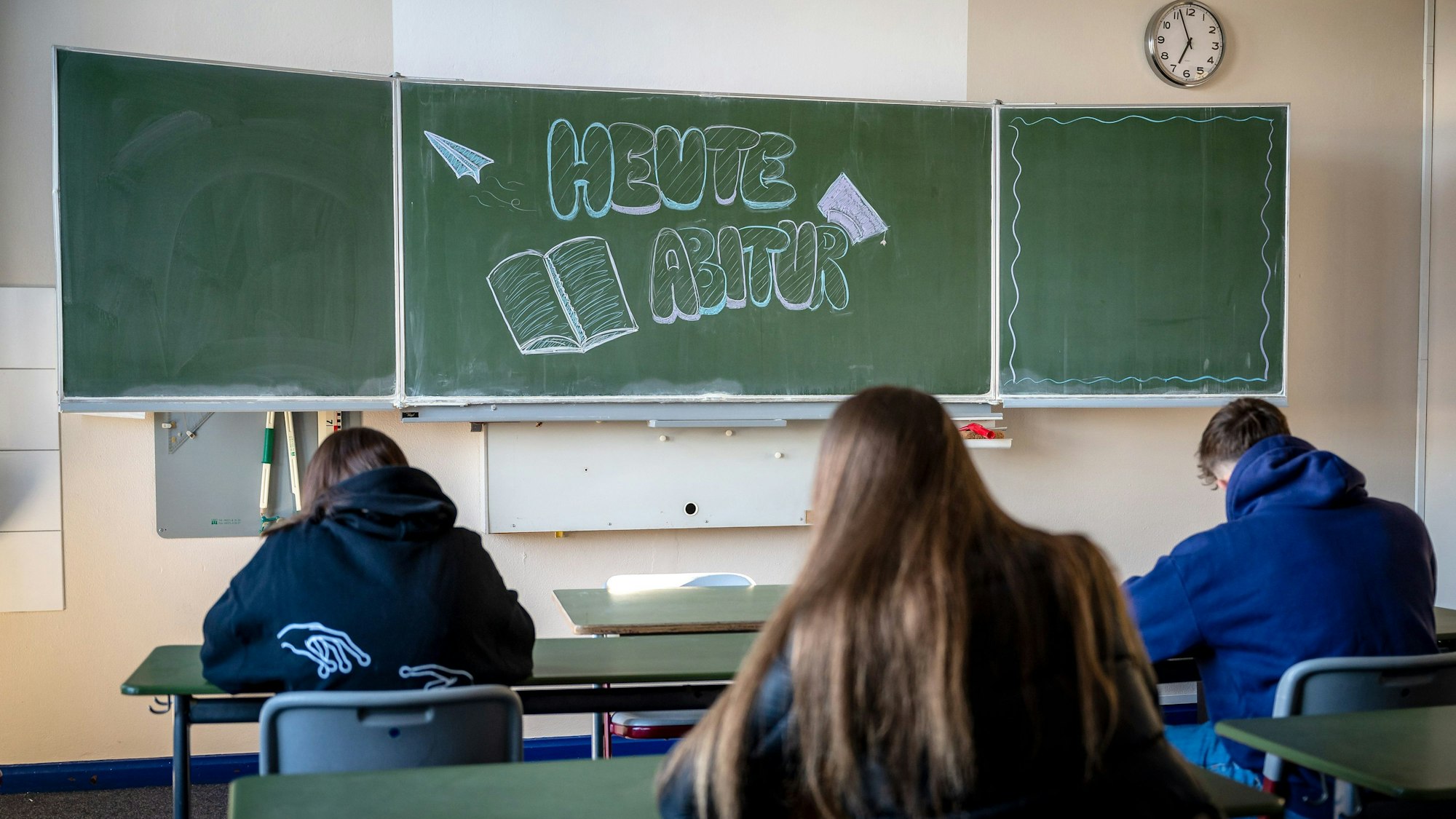 „Heute Abitur“ steht auf einer Tafel, vor der mehrere Schüler sitzen.