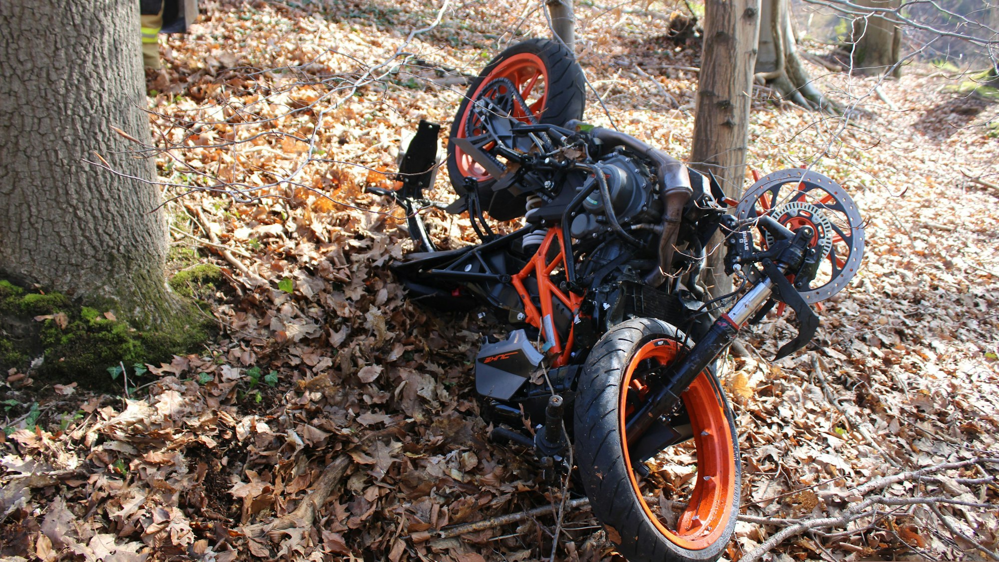 Ein schwer beschädigtes Motorrad liegt zwischen Bäumen in einem Wald.