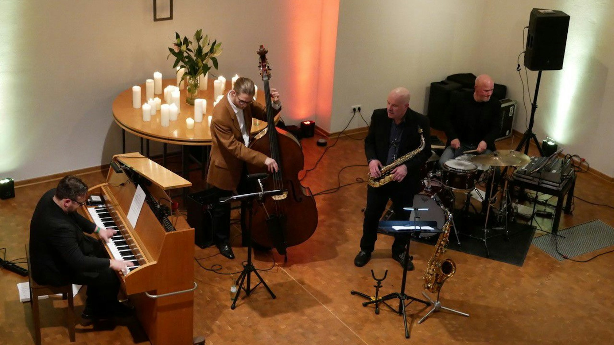 Vier Musiker sind zu sehen: Ein Pianist, ein Kontrabassist, ein Mann mit Saxofon und einer sitzt am Schlagzeug.